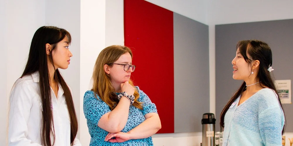 Three young people talk in a meeting room.