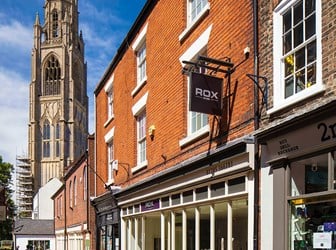 Narrow cobbled street with shop fronts leading towards a church tower.