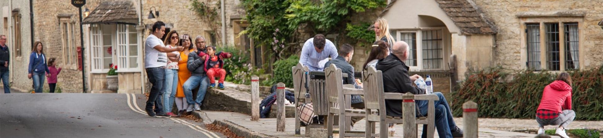 People sitting on benches with stone cottages in the background