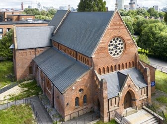 An exterior view of the west elevation of a Church from above with the Manchester skyline in the background. 