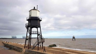 Iron framed lighthouse to the left and in the foreground with the sea in the background 