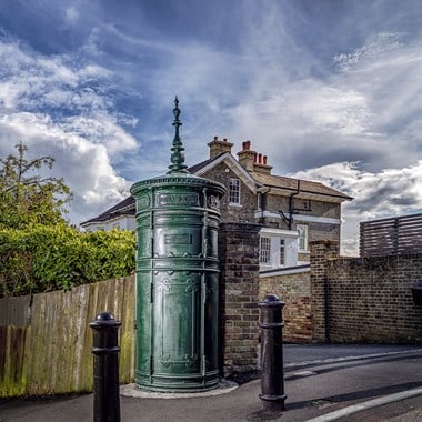 Late 19th-century cast iron cylindrical electricity substation with three rows of moulded cast iron patterned panels, projecting cornice, and foliated finial. 