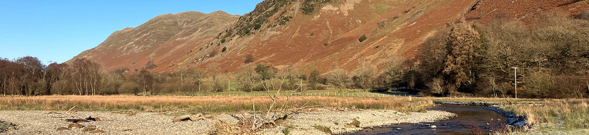  Modern colour photograph shows a section of re-wiggled river in a valley, with steep mountains rising in the distance. 