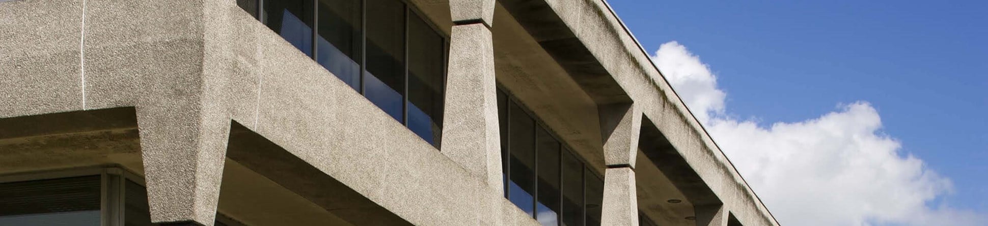 Three storey grey concrete modern building with grass lawn in front and blue skies.