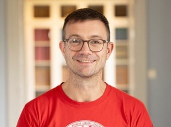 A head and shoulders portrait photograph of Jerome De Groot smiling in a red t-shirt