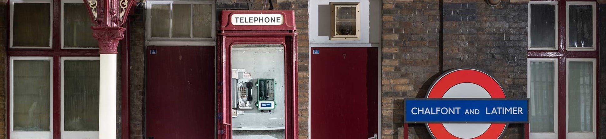 A telephone kiosk painted maroon on a railway station platform alongside seats.