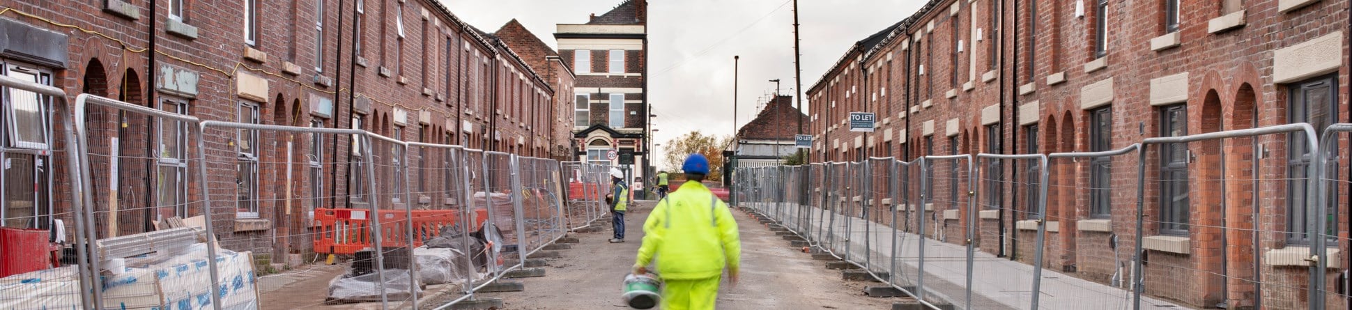 Street of terraced housing under building works with builders on site.