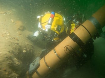 Diver holds a tube that is removing sand from the surface of the 'Rooswijk' wreck.