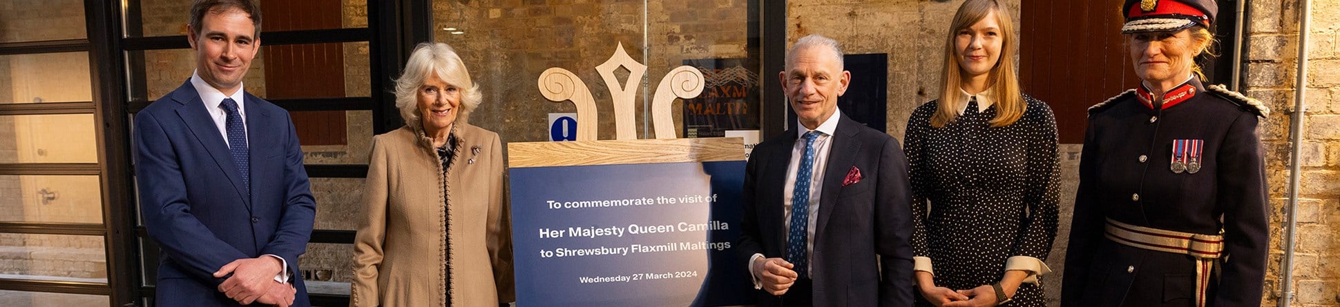 A photograph of five people stood next to a plaque being unveiled on a wooden easel