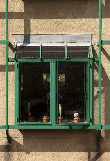 Metal framed window in a rendered wall. On the window sill are 4 cacti in pots.